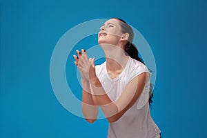 Studio portrait of a young beautiful woman in a white t-shirt against a blue wall background. People sincere emotions.