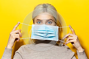 Studio portrait of a young blonde girl holding a medical flu mask on face, on yellow background.