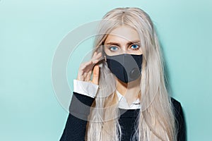 Studio portrait of young blonde girl wearing black respiratory face mask against coronavirus on aqua menthe color.