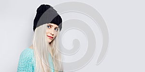 Studio portrait of young blonde girl on white background with copy space. Wearing black hat and cyan sweater