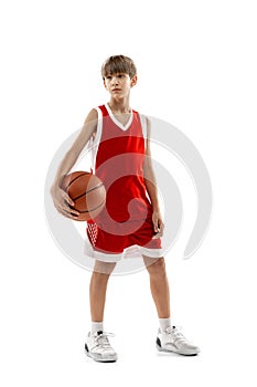 Studio portrait of young boy, basketball player in red uniform posing isolated over white background