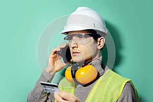 Studio portrait of young builder man, engineer, pay with credit card by phone. Wearing construction safety helmet.