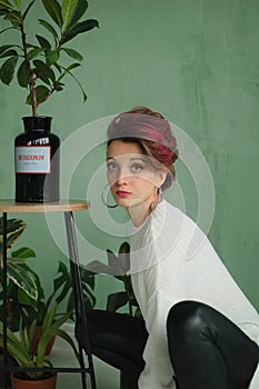 Studio portrait of young fashion model wearing white sweater and black leather leggings possing at studio with green