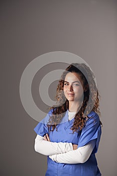 Studio Portrait Of Young Female Nurse Wearing Scrubs Standing Against Grey Background