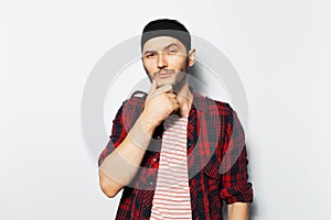 Studio portrait of young funny guy keeps hand on chin on white background.