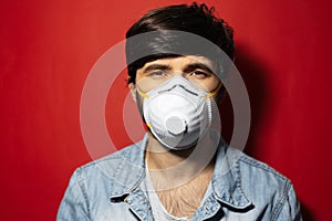 Studio portrait of young guy protect himself from coronavirus with medical flu mask on background of red color.