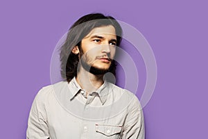 Studio portrait of young handsome man, with long brunette hair and beard. On the background of purple wall.