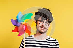 Studio portrait of a young man holding a windmill on a yellow background.
