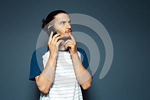 Studio portrait of young handsome thoughtful man, holding a smartphone.