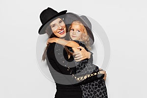 Studio portrait of young happiness pregnant woman hugging her daughter on white background. Wearing hats, dressed in black.