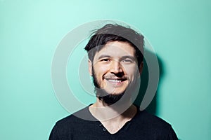 Studio portrait of young happy bearded hipster with disheveled hair and beard on background of aqua menthe color.