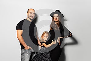 Studio portrait of young happy family, on white background. Wearing hat, dressed in black. Daughter hugging the belly.