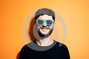 Studio portrait of young happy man, wearing aqua menthe or cyan sunglasses and black sweater on orange background.