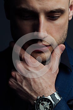 Studio portrait of young man in black shirt, holding hands in chin, looking down with humility.