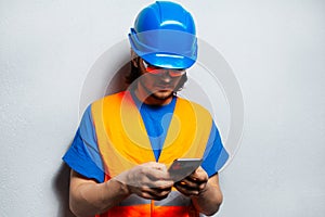 Studio portrait of young man, construction worker engineer, using smartphone wearing safety equipment on the background of grey.