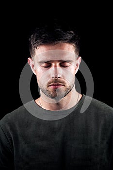 Studio Portrait Of Young Man With Serious Expression And Closed Eyes Against Black Background