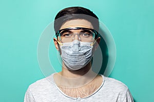 Studio portrait of young man wearing medical flu mask and safety goggles against coronavirus. On background of aqua menthe.
