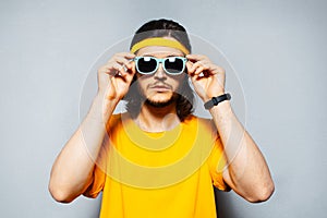 Studio portrait of young man wearing sunglasses, yellow band for head and shirt on background of grey textured wall.