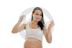 Studio portrait of young pregnant brunette woman with little socks in her hands isolated on white background