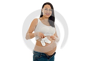 Studio portrait of young pregnant brunette woman with little socks in her hands smiling on camera isolated on white