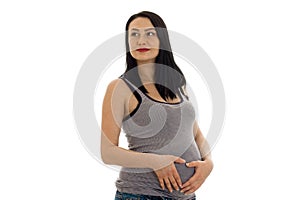 Studio portrait of young pregnant brunette woman in shirt touching her belly and looking aside isolated on white