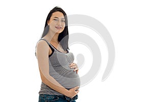 Studio portrait of young pregnant brunette woman in shirt touching her belly and looking at the camera isolated on white