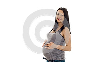 Studio portrait of young pregnant brunette woman in shirt touching her belly and smiling on camera isolated on white