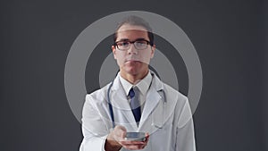 Studio portrait of young professional medical doctor using smartphone device over grey background