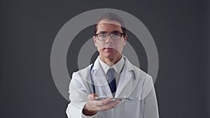Studio portrait of young professional medical doctor using smartphone device over grey background