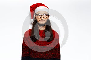 Studio portrait of young sad man in red sweater, wearing Santa Claus hat and eyeglasses. Isolated on white background.