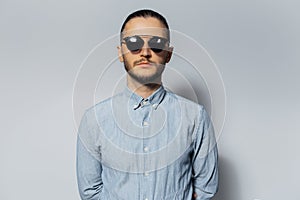 Studio portrait of young serious man wearing sunglasses and blue shirt on white background