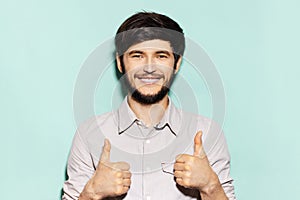 Studio portrait of young smiling guy showing thumbs up on background of aqua menthe color.