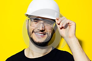 Studio portrait of young smiling man architect, builder engineer, wearing black sweater, touching his white construction safety he