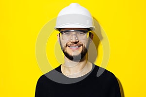 Studio portrait of young smiling man architect, builder engineer, wearing black sweater, white construction safety helmet and glas