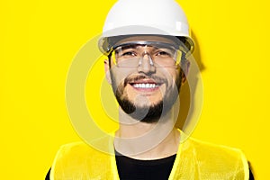 Studio portrait of young smiling man architect, builder engineer, wearing construction safety goggles, hard helmet.