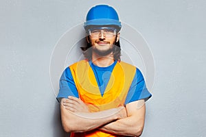 Studio portrait of young smiling man with crossed arms, construction worker engineer wearing safety equipment, hard hat, goggles.