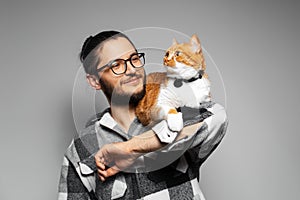 Studio portrait of young smiling man with red cat on his arms. Grey background