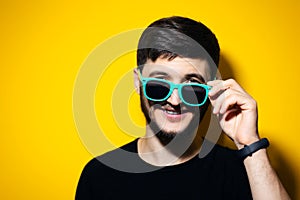 Studio portrait of young smiling man takes off his sunglasses on yellow background.