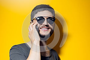 Studio portrait of young smiling man using smartphone, wearing sunglasses on yellow background.