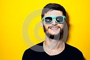 Studio portrait of young smiling man wearing sunglasses on yellow background.