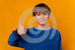 Studio portrait of a young smiling teen boy wearing blue showing thumb up.