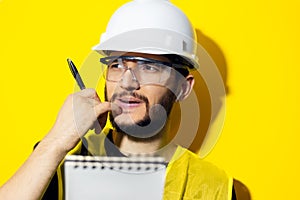 Studio portrait of young thinking man, builder engineer wearing safety helmet and glasses for construction on yellow background.