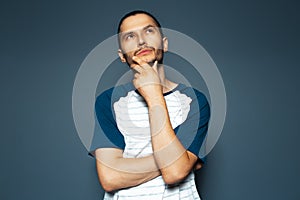 Studio portrait of young thoughtful man looking up with hand under chin on blue background