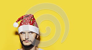 Studio portrait of young thoughtful man looking up, wearing Santa Hat. Background of yellow color with copy space. Christmas.