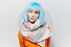 Studio portrait of young woman with blue hairstyle in orange sweater, wearing scarf. On white background.