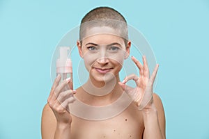 Studio portrait of a young woman holding a bottle of gentle foam facial cleanser. Beauty products and skin care concept.