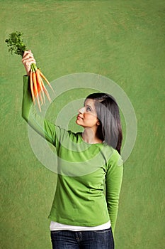 Studio portrait of a young woman holding up and looking at a bundle of carrots.