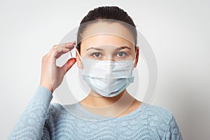 Studio portrait of young woman wearing a face mask, looking at camera, close up, isolated on gray background. Flu epidemic, dust