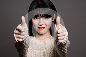 Studio portraits of happy twenties Asian women with thumbs up