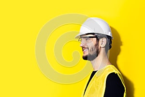 Studio profile portrait of young smiling man architect, builder engineer, wearing white construction safety helmet, glasses and ye